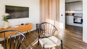 Et moderne køkken med stålemfang, et spiseområde i træ med et bord og stole, og et stort abstrakt maleri på væggen.