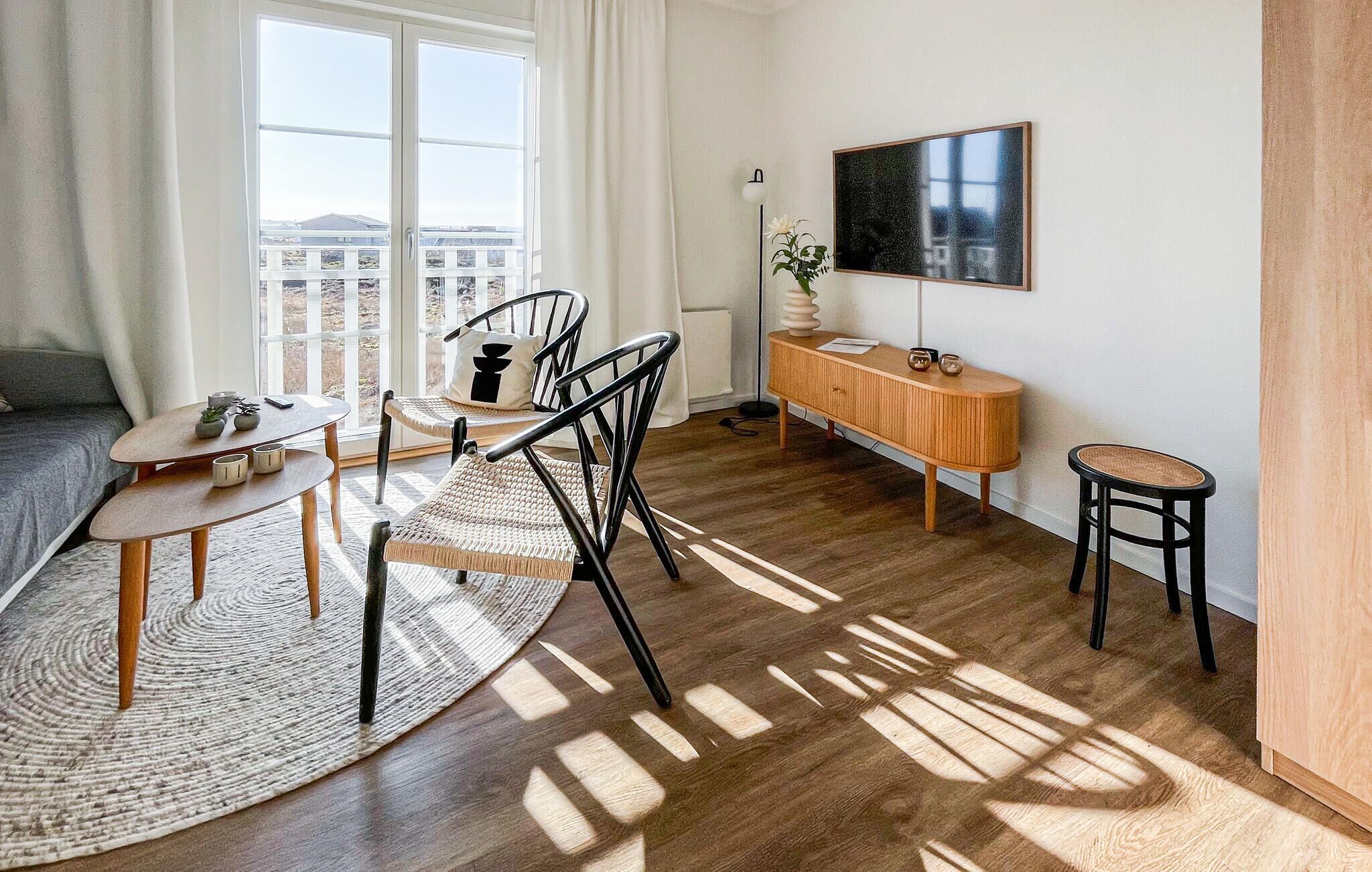 Ein modernes Wohnzimmer mit Essbereich, einer Couch, einem Couchtisch, einem Beistelltisch, einem Schrank und einem großen Fenster.