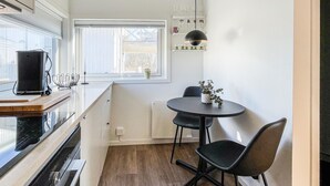 Et kompakt køkken med et vindue, et lille spisebord med stole og en hængende lampe.