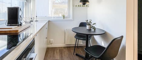 A compact kitchen with a window, a small dining table with chairs, and a pendant light.