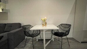 Ein kleiner Essbereich mit einem weißen Tisch und zwei schwarzen Stuhlgestellen. Auf dem Tisch steht eine Vase mit Kerzen und gelben Blumen.