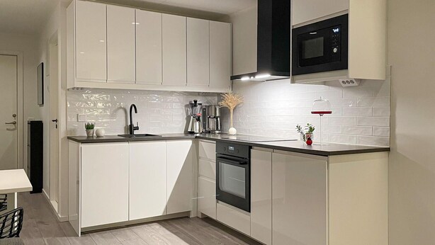 Eine moderne Küche mit weißen Schränken, einer schwarzen Mikrowelle und einem eingebauten Backofen.