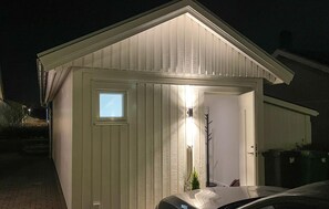 Ein kleines, eingeschossiges Gebäude mit einem geneigten Dach, einer Tür mit Fenster und einer Lampe an der Außenwand.