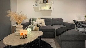 Ein modernes Wohnzimmer mit einem grauen Ecksofa, einem runden Couchtisch und einem schwarzen Teppich.