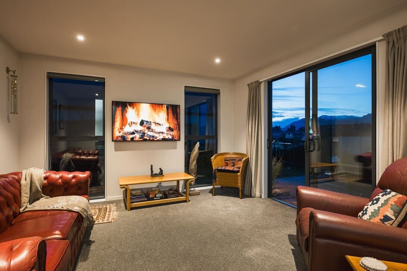 A living room with a fireplace, leather sofas, a television, and a view of the outdoors.