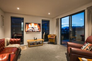 A living room with a fireplace, leather sofas, a television, and a view of the outdoors.