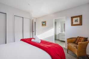 A hotel room with a bed, a red blanket, a white towel, a wicker chair, and a painting on the wall.