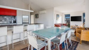 A modern kitchen with white cabinets, a red accent wall, and a dining area with a glass table and white chairs.