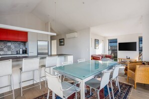 A modern kitchen with white cabinets, a red accent wall, and a dining area with a glass table and white chairs.
