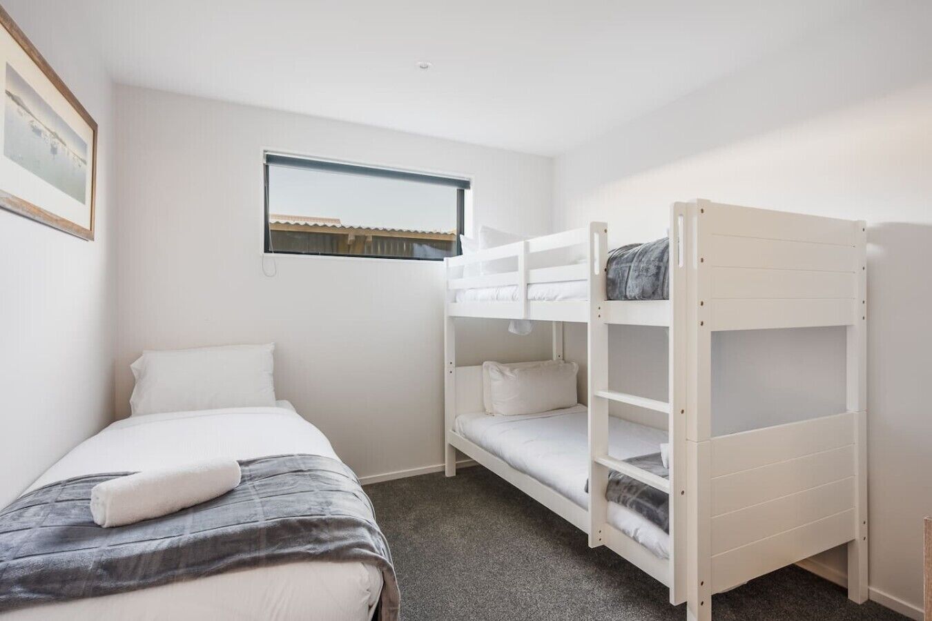 Een kamer met een eenpersoonsbed, een stapelbed, een raam en een lijst met een afbeelding aan de wand.