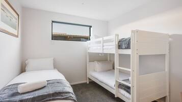 Een kamer met een eenpersoonsbed, een stapelbed, een raam en een lijst met een afbeelding aan de wand.