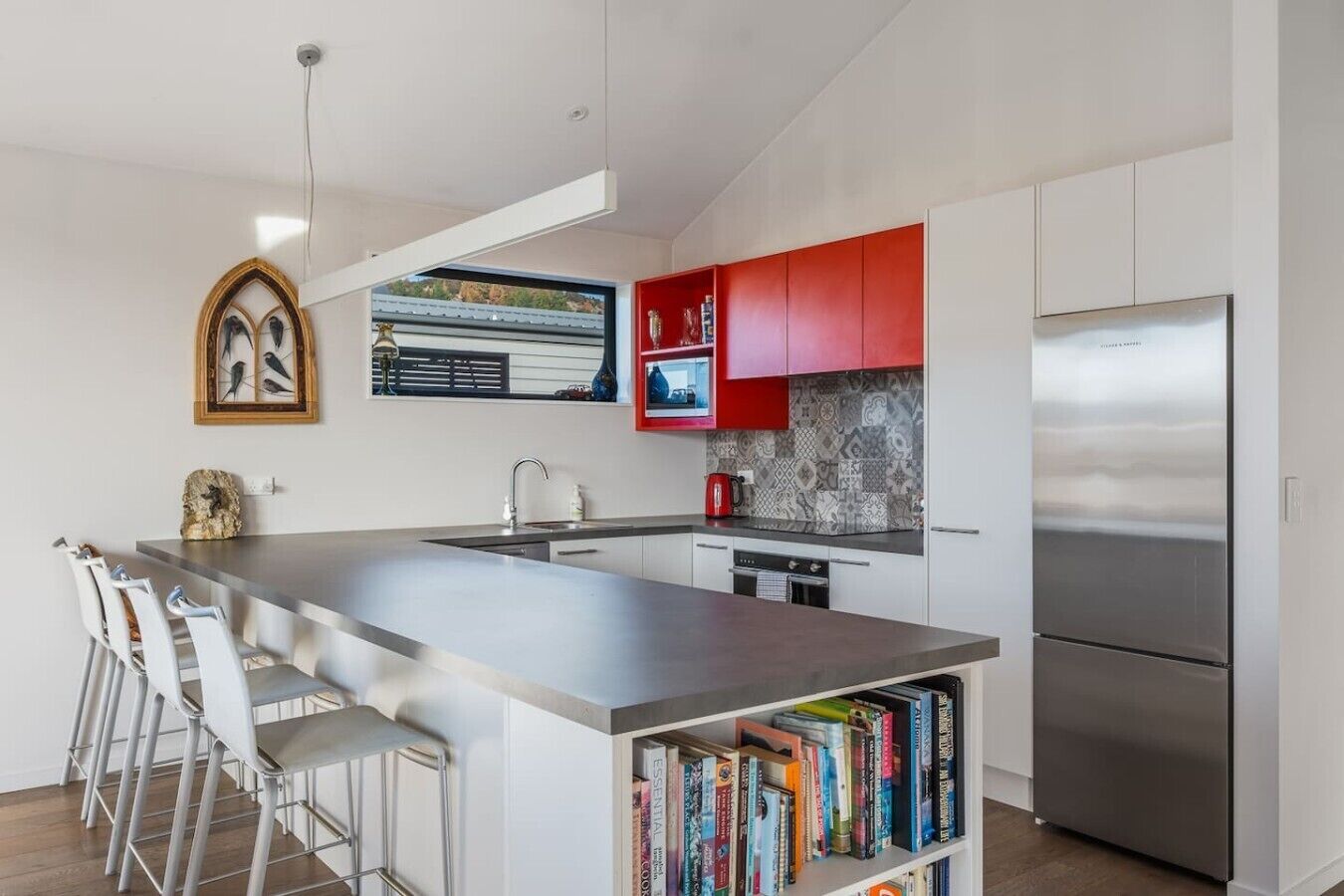 A modern kitchen with a central island, stainless steel appliances, and a red backsplash.