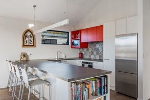 A modern kitchen with a central island, stainless steel appliances, and a red backsplash. - 3BR Wanaka Home Walkable Location Alpine Views (Wānaka)
