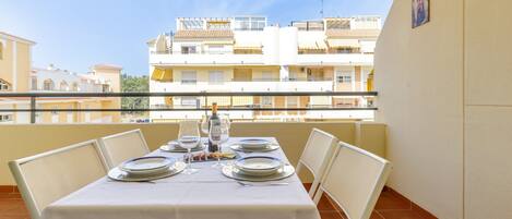 Un balcon avec une table dressée pour le dîner, donnant sur un quartier résidentiel composé de plusieurs immeubles.
