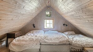 A room with a sloped ceiling, a window, a bed with multiple pillows, a bedside table, and a lamp. - Stunning home in Visby with WiFi (Visby)