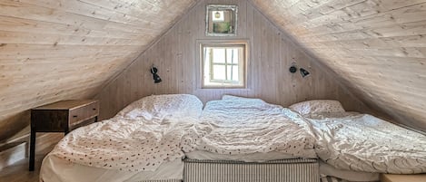 Une pièce avec un plafond en pente, une fenêtre, un lit avec plusieurs oreillers, une table de chevet et une lampe.