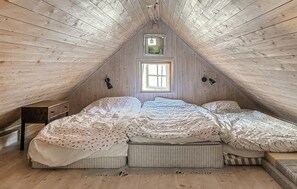 Ein Zimmer mit schrägem Dach, einem Fenster, einem Bett mit vielen Kissen, einem Nachttisch und einer Lampe.
