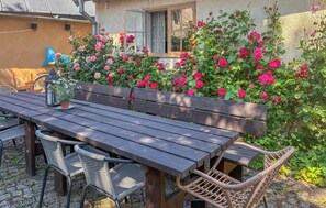 Eine Terrasse im Freien mit einem Holztisch und -stühlen, umgeben von einem Rosengarten in voller Blüte.