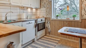 A compact kitchen with white cabinets, a dishwasher, an oven, and a window with a view of trees.