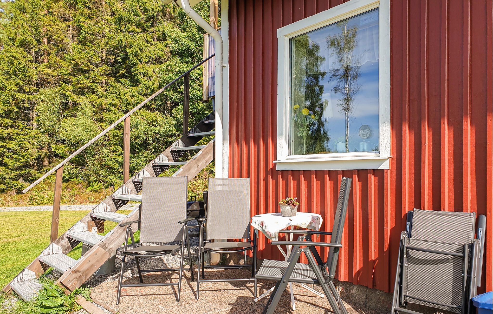 En röd byggnad med ett fönster, utomhusmöbler med stolar och ett bord, och en trappa som leder till entrén.