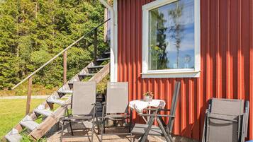 En röd byggnad med ett fönster, utomhusmöbler med stolar och ett bord, och en trappa som leder till entrén.