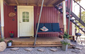A wooden porch with a white door, a bench with cushions, and a small outdoor grill. - Gorgeous apartment in Alingsås with WiFi (Alingsås)