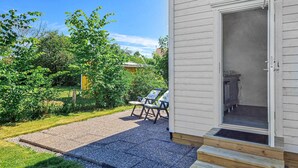 Een terras met een grindpad, een houten terras en een deur naar een kamer waar een keuken zichtbaar is.