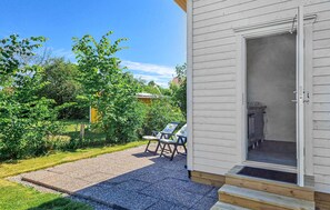 Eine Terrasse mit Kiesweg, einer Holzdielenveranda und einer Tür zu einem Raum, in dem eine Küche zu sehen ist.