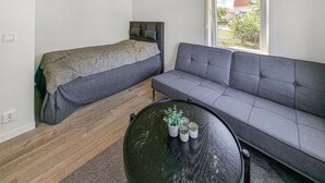 Een compacte kamer met een bed, een grijze bank en een ronde tafel met een bloempot.