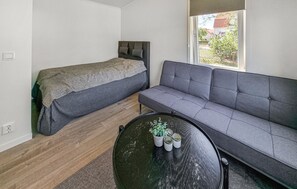 Ein kompakter Raum mit einem Bett, einem grauen Sofa und einem runden Tisch mit einer Topfpflanze.