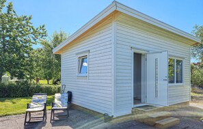 A small, single-story cabin with a door open, a window, and a table with chairs outside.