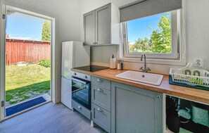 Eine kleine Küche mit Backofen, Spüle und Fenster mit Blick auf einen Garten.