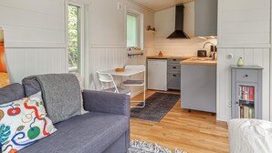 Ett kompakt vardagsrum med en grå soffa, ett litet matbord, en liten köksdel och en bokhylla.