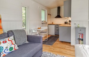A compact living space with a grey sofa, a small dining table, a kitchenette, and a bookshelf. - Nice home in Vänersnäs with house a mountain view (Vänersnäs)