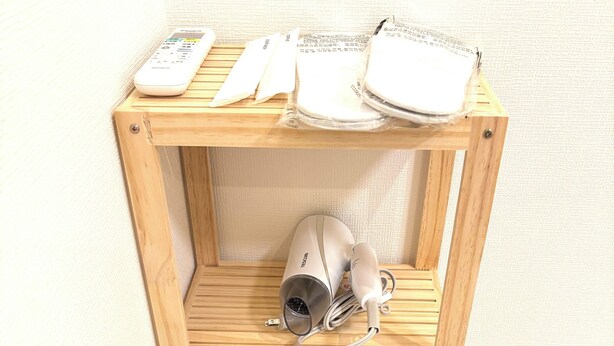 Une étagère en bois sur laquelle se trouvent un sèche-cheveux, un rouleau de papier toilette et deux tasses.