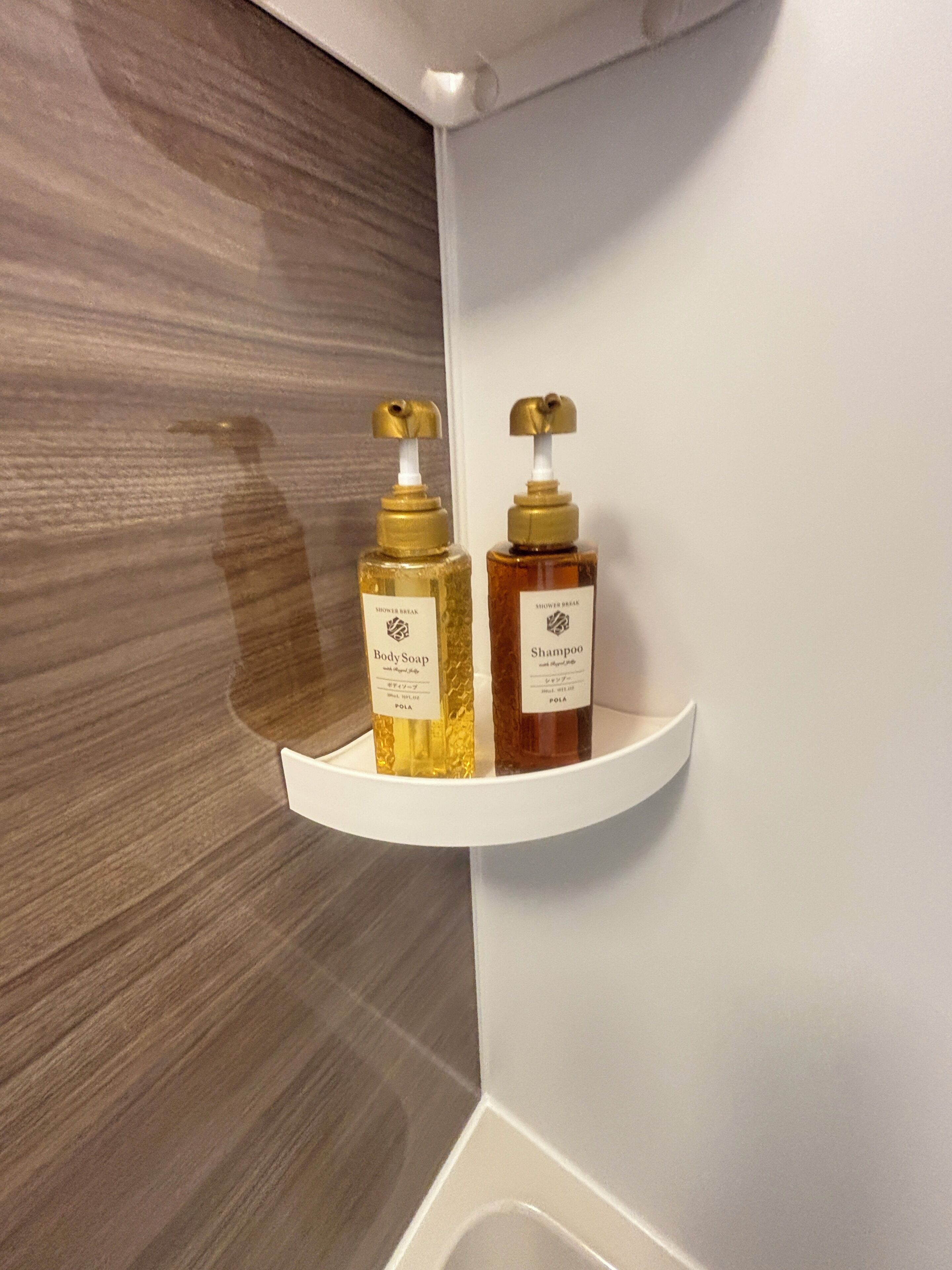 A bathroom with a white shelf holding two bottles of body soap and shampoo.