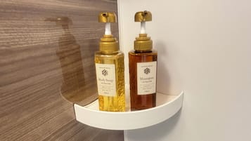 A bathroom with a white shelf holding two bottles of body soap and shampoo.