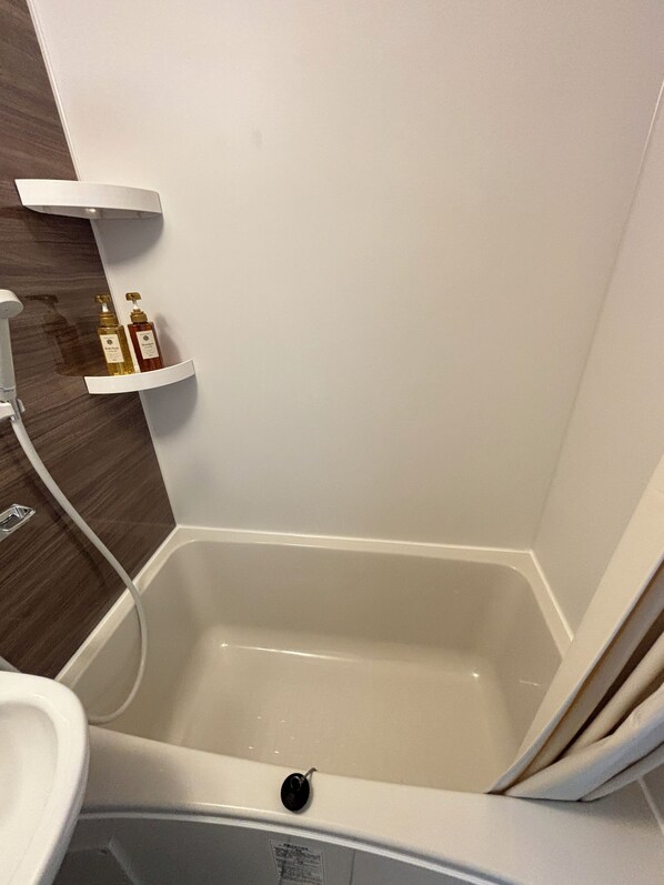 A bathroom with a bathtub, a shower, and a sink. There are two bottles on a shelf above the bathtub. - New Happy Smile (Tokyo)