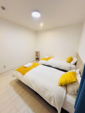 A hotel room with two beds, a small wooden shelf, and a ceiling light.