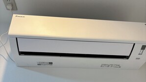 Un climatiseur Daikin blanc, fixé au mur, avec un câble d’alimentation visible.
