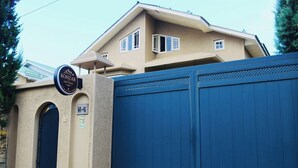 A guest house with a beige exterior, a blue gate, and a sign indicating it is a guest house. - Kohzar (Budgam)