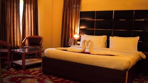 A hotel room with a bed, a chair, a bedside table, and a lamp. - Kohzar (Budgam)