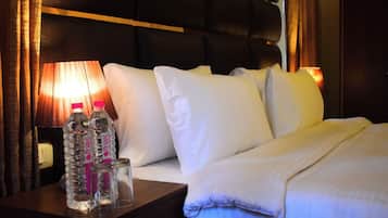 A hotel room with a bed, pillows, a nightstand with water bottles, and a lamp.