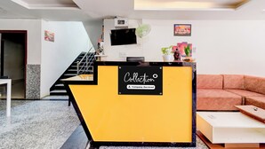 Ein Empfangsbereich mit gelbem Tresen, einer Treppe, einer Couch und einem Wandfernseher.