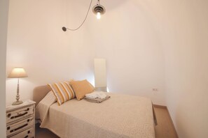 Quarto com cama, mesa de cabeceira, luminária, espelho e cômoda.