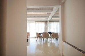 Ein moderner Essbereich mit Tisch und Stühlen, einem großen Fenster mit Vorhängen und einer Decke mit freiliegenden Balken.