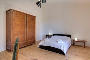 A bedroom with a large wooden wardrobe, a bed with white linens, two bedside tables with lamps, and a wooden floor. - Le Mortinete Farmstay: Moraiolo (Toscana)