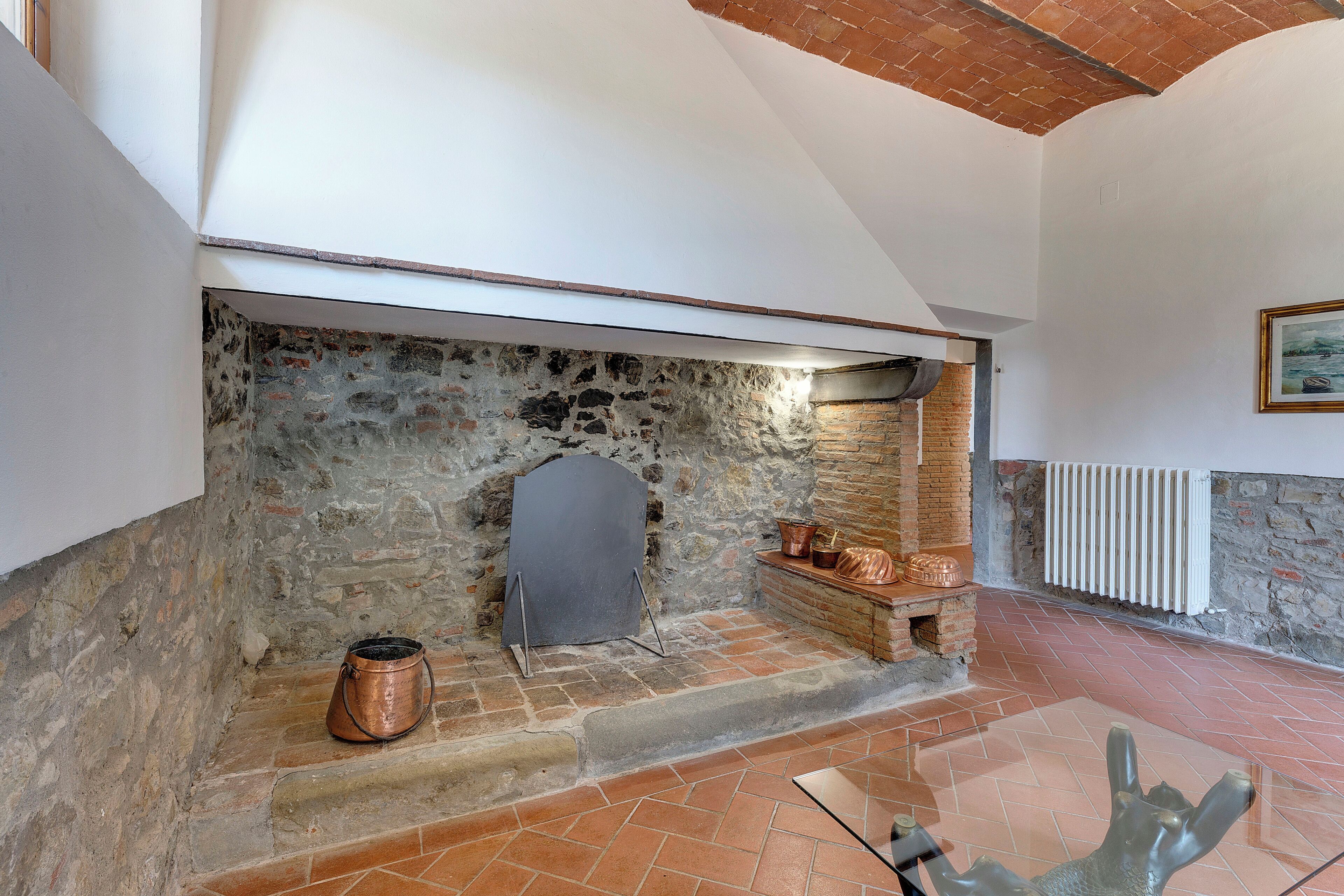 A stone fireplace with a white mantel, a copper pot, and a copper pot lid on a brick ledge.