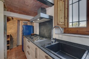 A kitchen with a gas stove, stainless steel sink, and wooden cabinets. - Le Mortinete Farmstay: Moraiolo (Toscana)