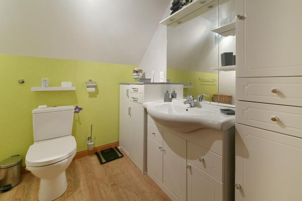 A bathroom with a toilet, sink, cabinets, and a mirror.